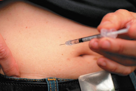 A photo shows a person holding a syringe up to his or her stomach, preparing to give an injection.